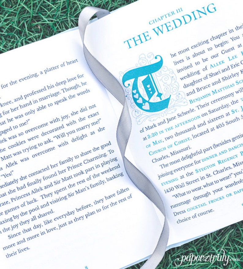 May include: A close-up of an open book with a silver ribbon bookmark. The book is titled "The Wedding" and features a blue and white illustration of a letter "T" with hearts. The text on the page describes a wedding ceremony and reception.