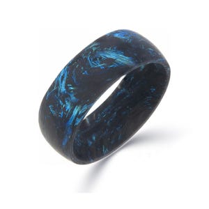 以下が含まれることがあります： 大理石模様の暗い色の指輪。指輪は黒を基調とし、青色の縞模様が入っています。耐久性のある素材で作られており、滑らかで丸みを帯びた形状をしています。この指輪はユニークなジュエリーです。