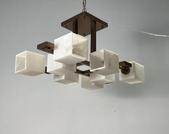 Könnte beinhalten: Ein moderner Kronleuchter mit geometrischem Design, der mehrere weiße, würfelförmige Leuchten aus Alabaster an einem dunklen bronzefarbenen Metallrahmen trägt.