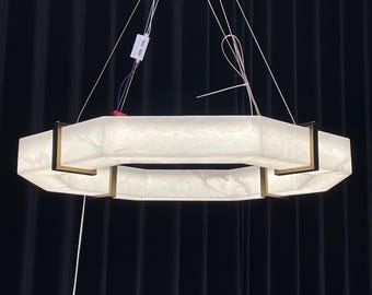 Könnte beinhalten: Ein moderner, achteckiger Kronleuchter mit einem weißen Alabaster-Schirm und goldenen Metallakzenten. Der Kronleuchter ist mit mehreren Drähten an der Decke befestigt.