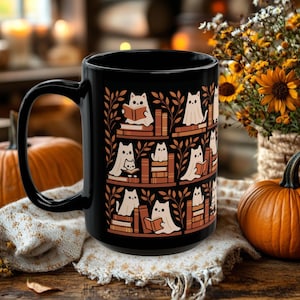May include: A black ceramic mug featuring a repeating pattern of white ghost-like cats sitting on shelves among stacks of books and leafy branches. The design is rendered in shades of orange, brown, and cream, contrasting against the dark mug surface.