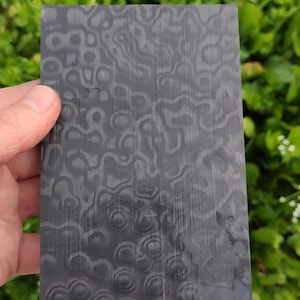 May include: A white ceramic mug with a black handle and the text "But First, Coffee" in a bold, black font. The mug is set against a blurred background, suggesting a cozy setting.