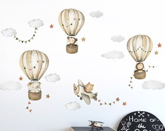 May include: A set of wall decals featuring hot air balloons with animals inside, clouds, stars, and a banner. The decals are in a watercolour style with brown, white, and orange colours. The text "Home of the Cool Kids" is written on a black chalkboard.