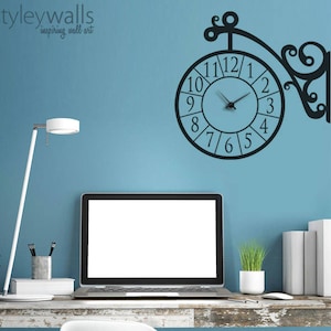May include: Black and white wall clock decal with a decorative design. The clock is mounted on a blue wall with a desk and a laptop in front of it.