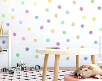 Puede incluir: Una pared blanca con puntos de acuarela de colores, una mesa blanca con base de madera, un taburete rosa y un ratón de peluche. El texto "styleywalls inspiring wall art" está en la esquina superior derecha de la imagen.