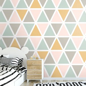 Può includere: Un muro bianco con un motivo geometrico di triangoli in tonalità di rosa, verde, grigio e giallo. Il muro è in una stanza con un letto bianco e una cassettiera in legno.