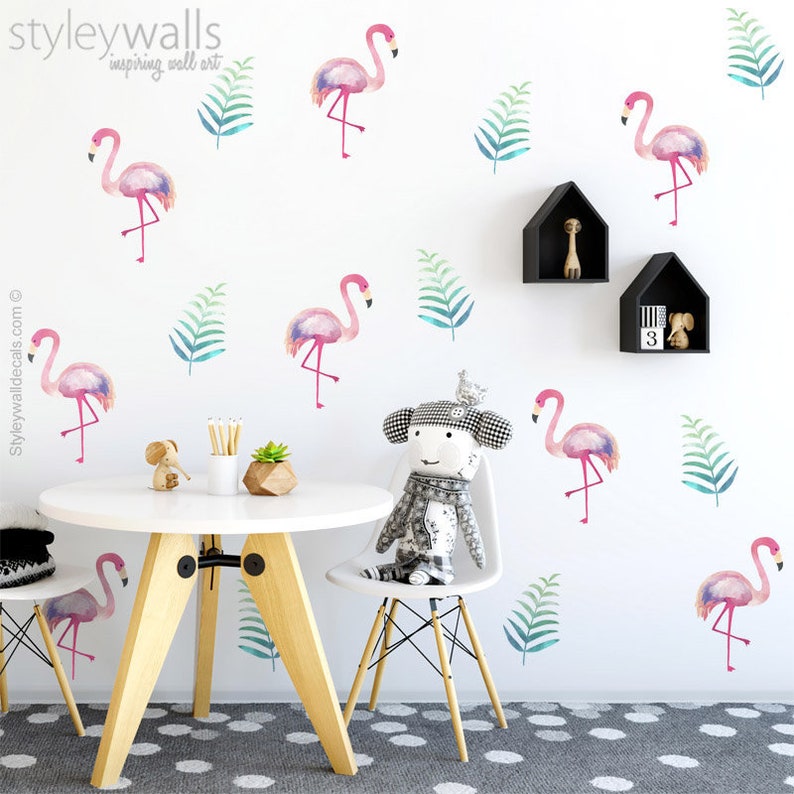 Puede incluir: Calcoman&iacute;as de pared de flamencos rosas con dise&ntilde;os de estilo acuarela, que representan hojas tropicales. Las calcoman&iacute;as se muestran en una pared blanca en una habitaci&oacute;n con una mesa y sillas.