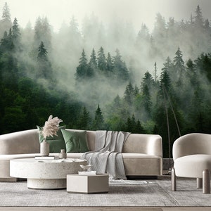 May include: A living room interior design with a white sectional sofa, a white coffee table, a white armchair, and a floor lamp. The wall behind the furniture features a large-scale photo mural of a misty forest.
