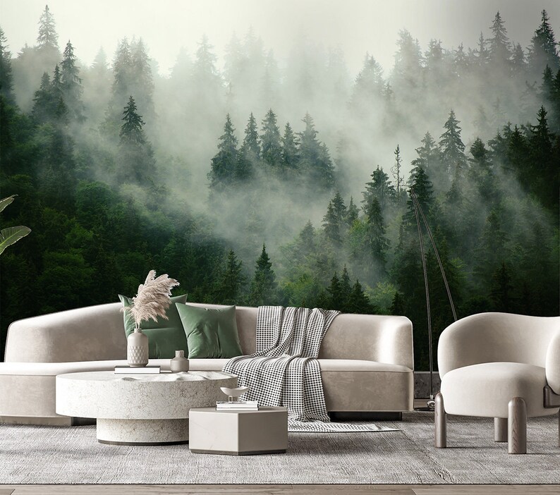 May include: A living room interior design with a white sectional sofa, a white coffee table, a white armchair, and a floor lamp. The wall behind the furniture features a large-scale photo mural of a misty forest.