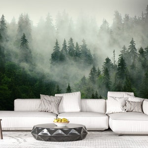 May include: A white sectional sofa with gray and white striped throw pillows sits in front of a wall mural depicting a misty forest. The sofa is positioned on a white rug with a black geometric coffee table in front of it.