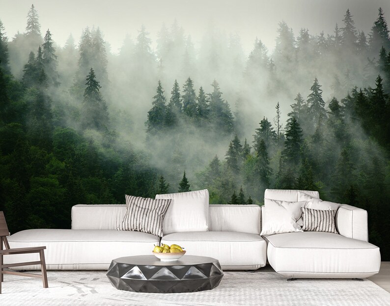 May include: A white sectional sofa with gray and white striped throw pillows sits in front of a wall mural depicting a misty forest. The sofa is positioned on a white rug with a black geometric coffee table in front of it.