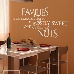 May include: A brown wall with a white vinyl decal that reads "Families are like fudge mostly sweet with lots of nuts". The decal is in a dining room with a brown table and chairs.