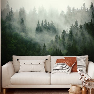 May include: A white sofa with two throw pillows and a brown throw pillow in front of a wall mural depicting a misty forest scene.