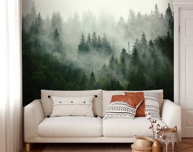 May include: A white sofa with two throw pillows and a brown throw pillow in front of a wall mural depicting a misty forest scene.