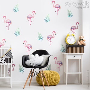 Puede incluir: Calcoman&iacute;as de pared de flamencos rosas con dise&ntilde;os de estilo acuarela, que presentan una variedad de poses y tama&ntilde;os. Las calcoman&iacute;as se muestran en una pared blanca con hojas verdes, una silla negra y un reloj amarillo.
