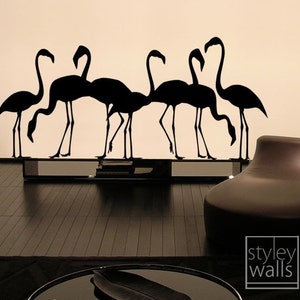 May include: Black silhouette wall decal of a flock of flamingos. The decal is applied to a white wall and is reflected in a black mirror surface below. The decal is part of a home decor collection.