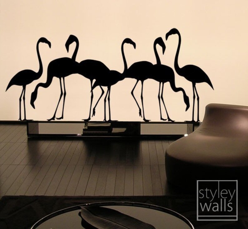 May include: Black silhouette wall decal of a flock of flamingos. The decal is applied to a white wall and is reflected in a black mirror surface below. The decal is part of a home decor collection.