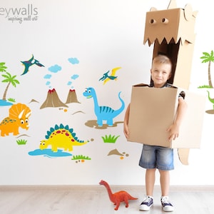 May include: A child wearing a cardboard dinosaur costume stands in front of a wall with dinosaur wall decals. The decals feature a variety of dinosaurs, including a triceratops, a stegosaurus, and a pterodactyl. There are also palm trees and volcanoes on the wall.