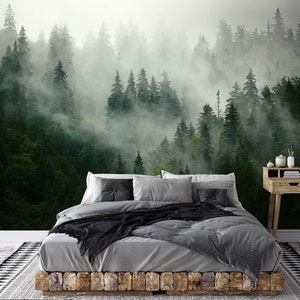 May include: A gray bed with a black throw blanket and gray pillows sits in front of a wall mural depicting a misty forest with green trees.