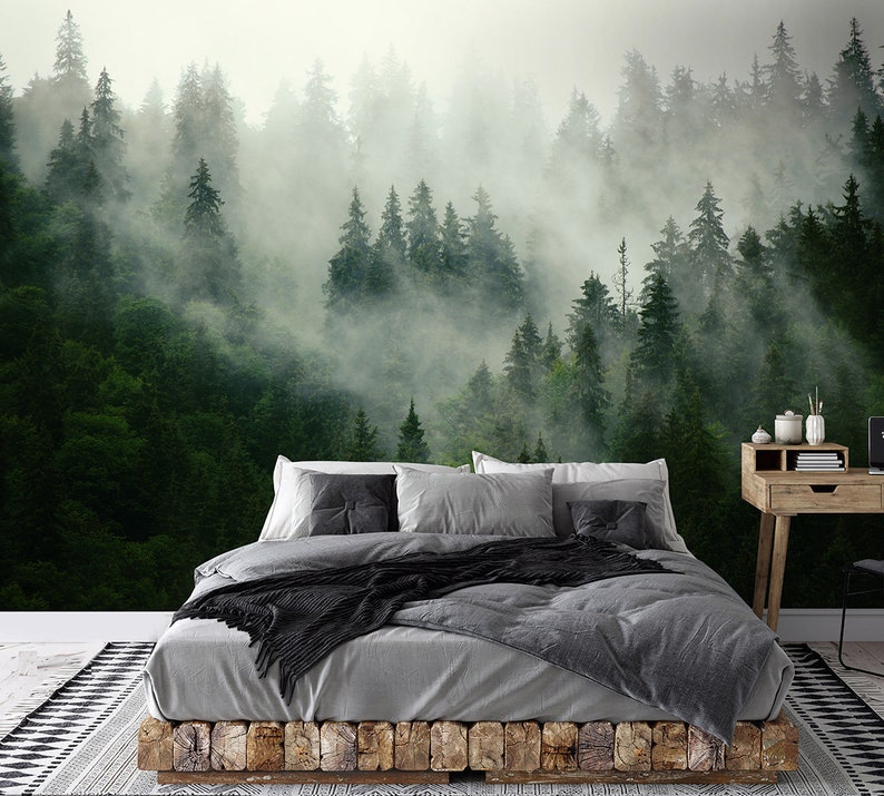 May include: A gray bed with a black throw blanket and gray pillows sits in front of a wall mural depicting a misty forest with green trees.