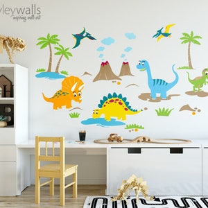 May include: A set of colorful dinosaur wall decals featuring a blue dinosaur, a yellow dinosaur, an orange dinosaur, a green dinosaur, two palm trees, two volcanoes, and a pterodactyl. The decals are on a white wall in a child's room.
