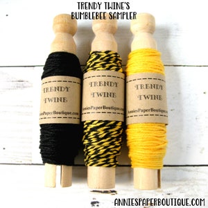 May include: Three spools of twine in black, yellow and black striped, and yellow. Each spool has a label that reads "TRENDY TWINE" and "AnniesPaperBoutique.com". The text "TRENDY TWINE'S BUMBLEBEE SAMPLER" is at the top of the image.