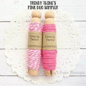 May include: Two spools of pink baker's twine, one solid pink and one white and pink striped, on a white doily. The spools are labeled "Trendy Twine" and "Annie's Paper Boutique.com".
