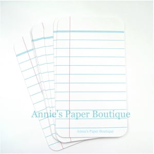 May include: A stack of blank note cards with blue and red lines. The cards are white and have the text "Annie's Paper Boutique" printed on the bottom.