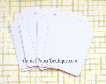 May include: A stack of ten white scalloped gift tags with a hole punched in the top corner. The tags are blank and ready to be written on. The text "AnniesPaperBoutique.com" is printed on the bottom of the tags.