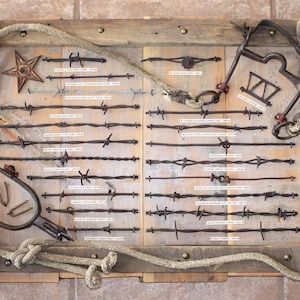 May include: A rustic wooden display board featuring various types of barbed wire, a metal star, and a spur. The board is framed with rope and has small labels identifying each wire type. The overall color scheme is brown and metallic.