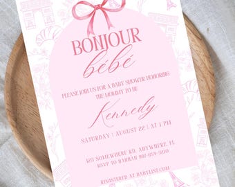Puede incluir: Una invitación de baby shower rosa y blanca con temática parisina. La invitación presenta un lazo rosa, la Torre Eiffel y el texto "Bonjour bebe". También incluye el texto "Por favor, únase a nosotros para una baby shower en honor a la futura mamá Kennedy".