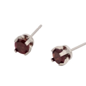 May include: A pair of silver stud earrings with small, round, dark red gemstones.