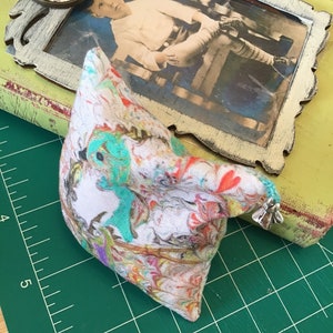 May include: A vintage photo of a young boy sitting in a chair is framed in a white frame with a distressed finish. The frame is on top of a green cutting mat. A small pillow with a colorful floral pattern is in the foreground.