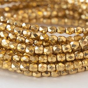 May include: A close-up of a strand of gold-colored faceted beads. The beads are small and round, and they are arranged in a circular pattern.