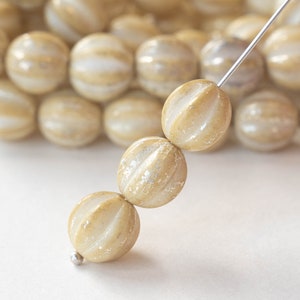 May include: A strand of cream-colored glass beads with a subtle shimmer. The beads have a ribbed texture and are strung on a silver wire.