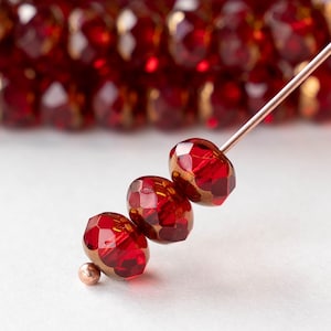 May include: Four red glass beads with gold accents strung on a wire. The beads are faceted and have a shiny finish.