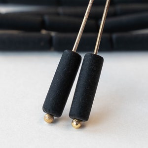 May include: A pair of black earrings with gold accents. The earrings are made of small black cylinders with gold tops.