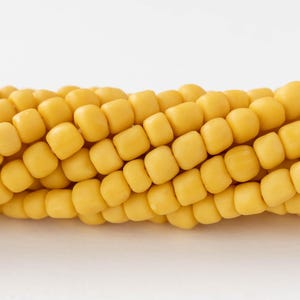 Op de afbeelding: Close-up van een verse maïskolf met heldergele korrels. De korrels zijn dicht op elkaar gepakt en gerangschikt in nette rijen, waardoor een textuur ontstaat. De maïs staat tegen een effen witte achtergrond, wat de natuurlijke kleur en vorm benadrukt.