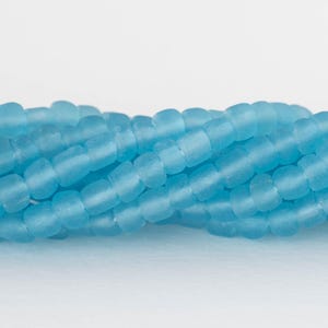 May include: A white ceramic mug with a black handle and the text "But First, Coffee" in a bold, black font. The mug is filled with a dark liquid, likely coffee, and sits on a light-colored surface.