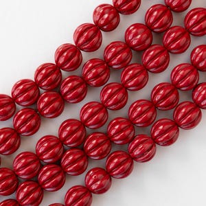 May include: A strand of red, round beads with a textured, ribbed surface. The beads are arranged in rows, creating a repeating pattern.