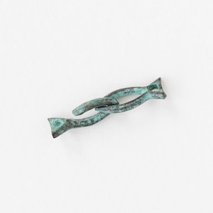 May include: A weathered, bronze-coloured metal link with a turquoise patina. The link has a unique, intertwined design with flared ends. The object is set against a plain white background, highlighting its aged appearance and intricate form.