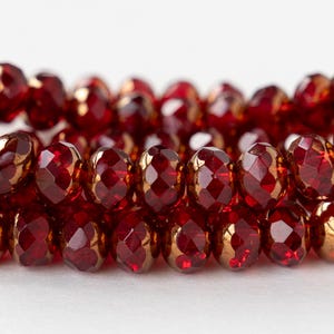 May include: A strand of red faceted glass beads with gold accents. The beads are round and have a shiny finish.