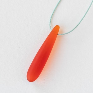 Puede incluir: Un colgante de l&aacute;grima de vidrio rojo en un cord&oacute;n azul claro.