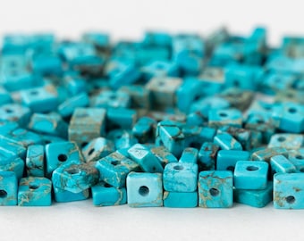 May include: A large pile of turquoise blue square beads with a hole in the center of each bead. The beads are made of natural stone and have a mottled appearance.