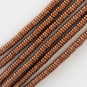 May include: A strand of copper-colored beads, each bead is a small, round coil. The beads are arranged in a diagonal line, with the top of the line extending to the right and the bottom of the line extending to the left.