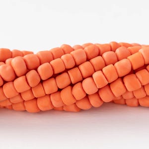 May include: Close-up of a section of orange beads, possibly for jewelry making. The beads are square-shaped and arranged in a row, with a slight curve. The background is plain white, highlighting the vibrant color and texture of the beads.