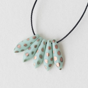 May include: A necklace with five teardrop-shaped beads. The beads are a light green color with gold polka dots.