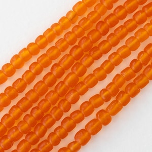Op de afbeelding: Een streng oranje glazen kralen, elke kraal is licht afgerond en heeft een matte afwerking.
