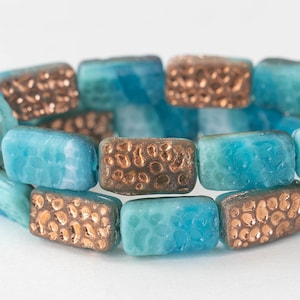 May include: A close-up of a bracelet made of turquoise and copper rectangular beads. The beads have a textured surface and are arranged in a repeating pattern.