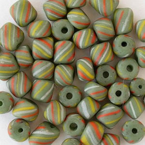 Può includere: Una collezione di perline di vetro verde oliva con strisce diagonali bianche, gialle e arancioni. Le perline hanno varie forme, tra cui quadrati arrotondati e cilindri, e presentano fori per l'infilatura. Adatte per la creazione di gioielli.